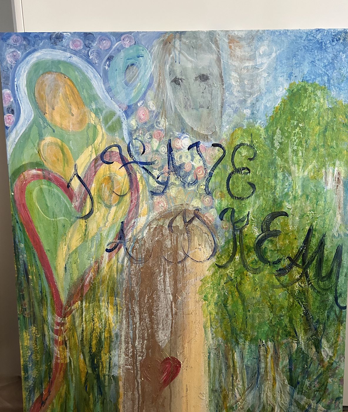 Målning med änglagestalt, hjärta och skrift i blått över grönska